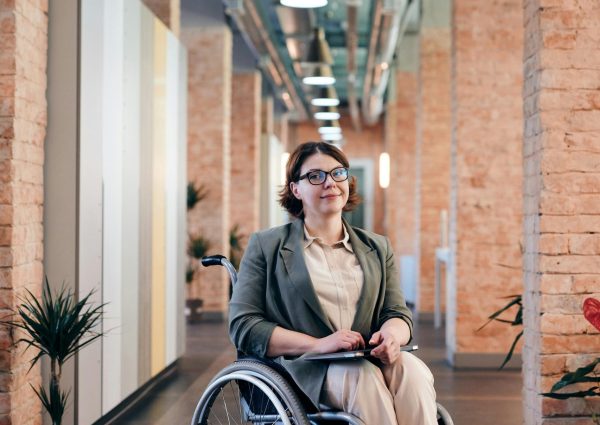 Confident businesswoman smiling while sitting in a wheelchair in a contemporary office setting.
